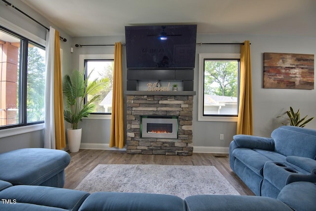 living room with a stone fireplace, a wealth of natural light, and light wood-type flooring