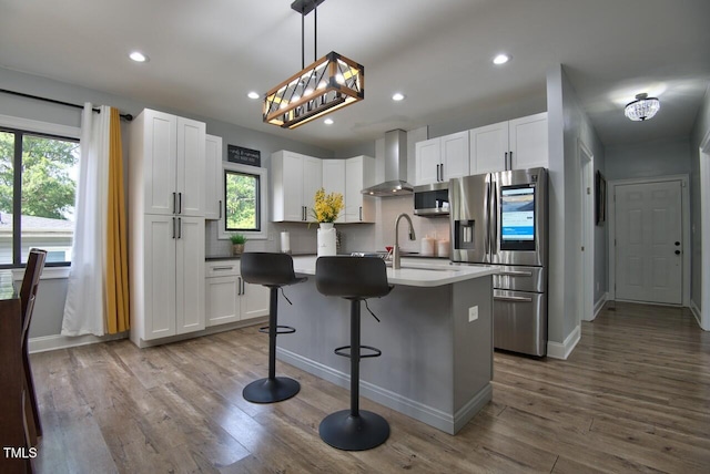 kitchen with stainless steel appliances, a center island with sink, wall chimney range hood, and white cabinets