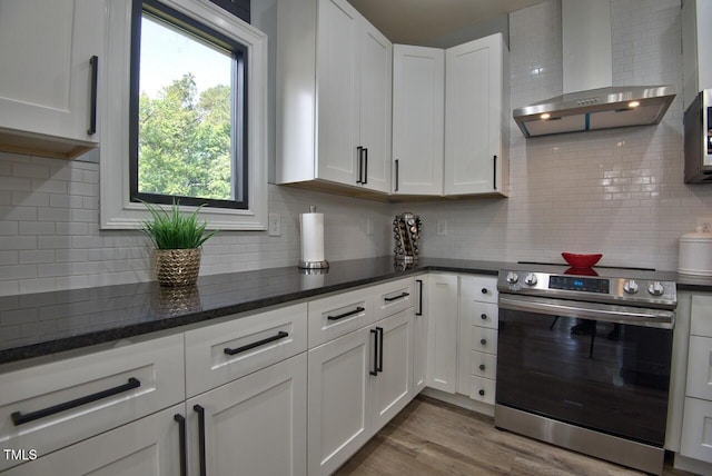 kitchen with electric stove, wall chimney range hood, light hardwood / wood-style flooring, white cabinets, and decorative backsplash