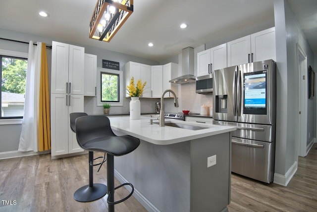 kitchen with white cabinetry, a kitchen breakfast bar, stainless steel fridge with ice dispenser, a center island with sink, and wall chimney exhaust hood