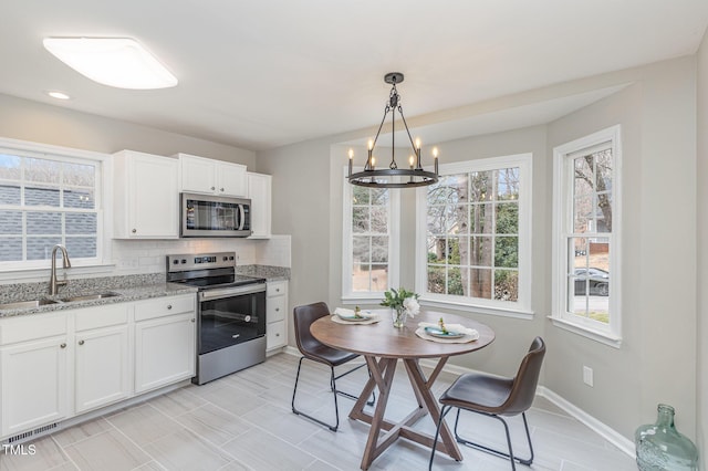 kitchen with appliances with stainless steel finishes, decorative light fixtures, sink, and white cabinets