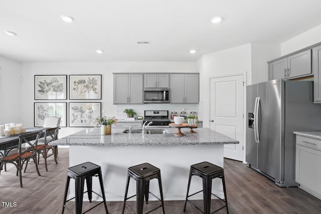 kitchen with light stone countertops, appliances with stainless steel finishes, sink, and a center island with sink