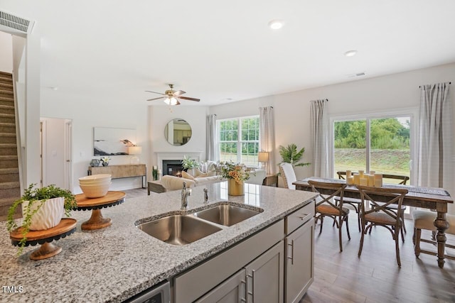 kitchen with sink, gray cabinetry, dark hardwood / wood-style floors, ceiling fan, and light stone countertops