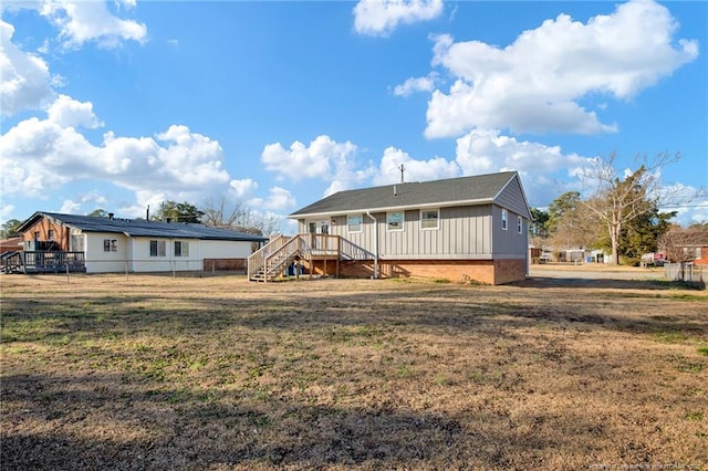 back of house featuring a lawn, board and batten siding, fence, a wooden deck, and stairs