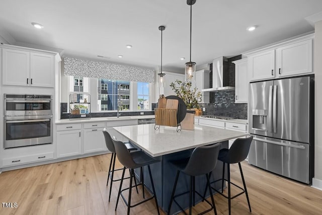 kitchen with white cabinetry, hanging light fixtures, stainless steel appliances, and wall chimney exhaust hood