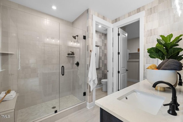 bathroom featuring a shower with shower door, tile walls, vanity, toilet, and tile patterned floors