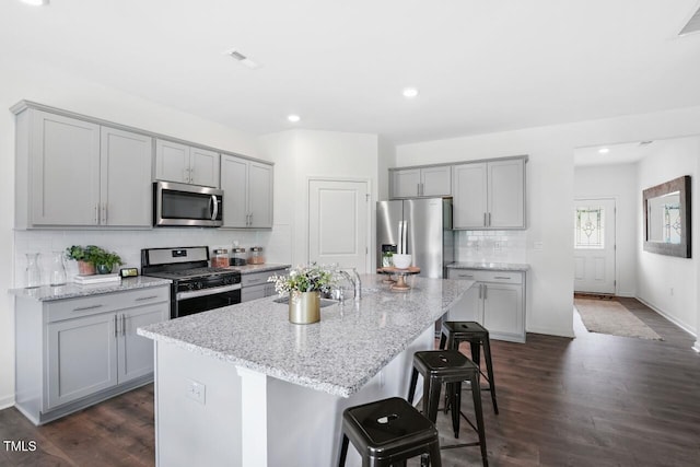 kitchen with stainless steel appliances, light stone countertops, a kitchen island with sink, and a breakfast bar area