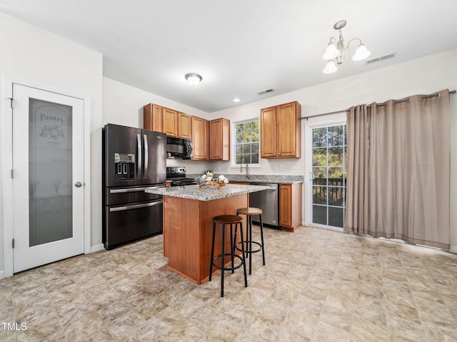 kitchen with visible vents, a center island, a kitchen bar, brown cabinetry, and black appliances