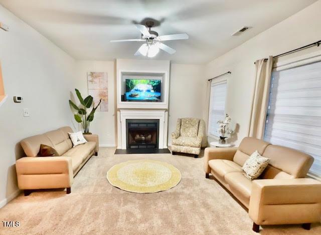 living area featuring carpet, a fireplace with flush hearth, a ceiling fan, visible vents, and baseboards