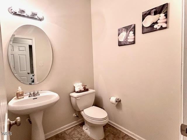 half bath featuring baseboards, a sink, and toilet