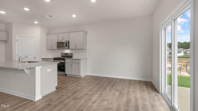 kitchen featuring appliances with stainless steel finishes, sink, gray cabinetry, a kitchen island with sink, and light stone countertops