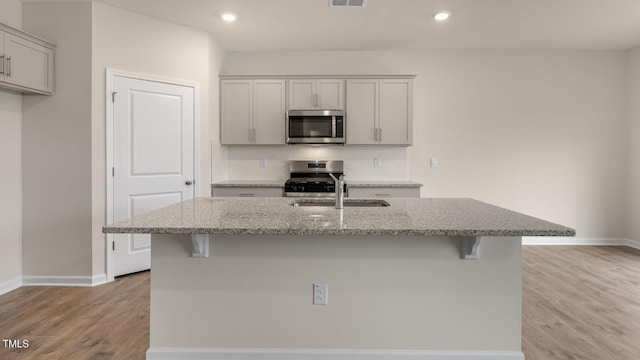 kitchen with stainless steel appliances, light stone countertops, gray cabinetry, and a center island with sink