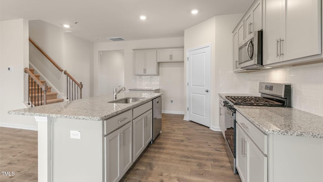 kitchen featuring sink, light stone counters, a center island with sink, light wood-type flooring, and stainless steel appliances