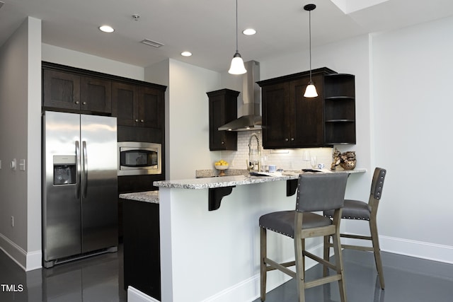 kitchen featuring wall chimney range hood, appliances with stainless steel finishes, a kitchen breakfast bar, baseboards, and tasteful backsplash