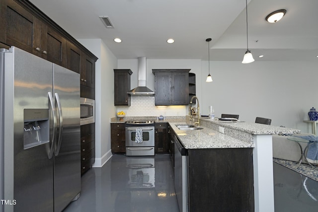kitchen featuring wall chimney range hood, tasteful backsplash, light stone counters, a sink, and appliances with stainless steel finishes