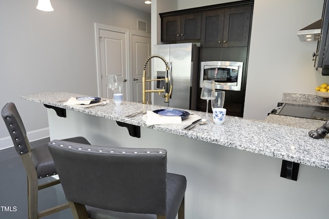 kitchen featuring visible vents, dark brown cabinetry, a breakfast bar, light stone counters, and stainless steel appliances