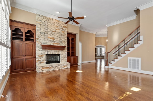 unfurnished living room featuring crown molding, ceiling fan, a stone fireplace, and hardwood / wood-style floors