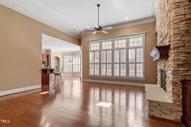 unfurnished living room with crown molding, wood-type flooring, a stone fireplace, and ceiling fan with notable chandelier