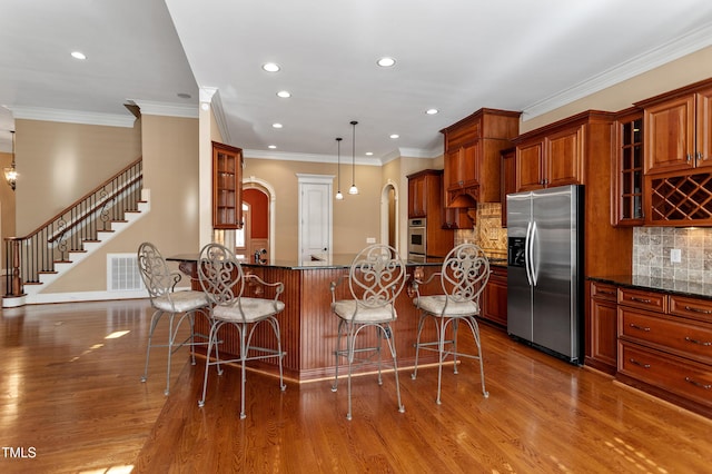 kitchen with pendant lighting, dark stone counters, stainless steel fridge with ice dispenser, and a breakfast bar area