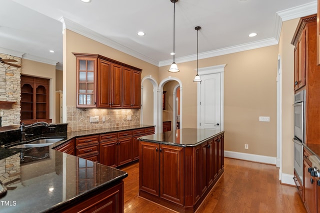 kitchen with pendant lighting, wood-type flooring, sink, dark stone countertops, and a center island