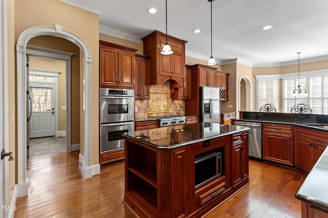 kitchen featuring a center island, dark stone counters, ornamental molding, pendant lighting, and stainless steel appliances