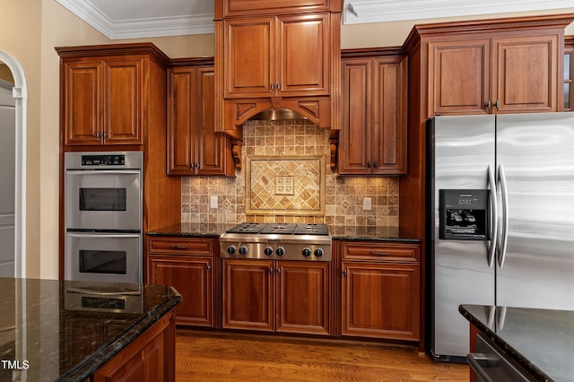 kitchen featuring crown molding, dark stone countertops, stainless steel appliances, dark hardwood / wood-style floors, and tasteful backsplash