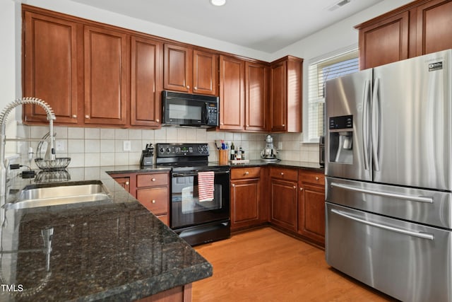 kitchen with sink, dark stone countertops, decorative backsplash, black appliances, and light hardwood / wood-style flooring