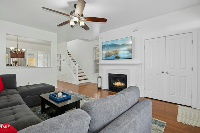 living room featuring hardwood / wood-style flooring, ceiling fan with notable chandelier, and a brick fireplace