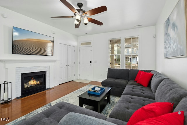 living room featuring hardwood / wood-style flooring, a brick fireplace, and ceiling fan