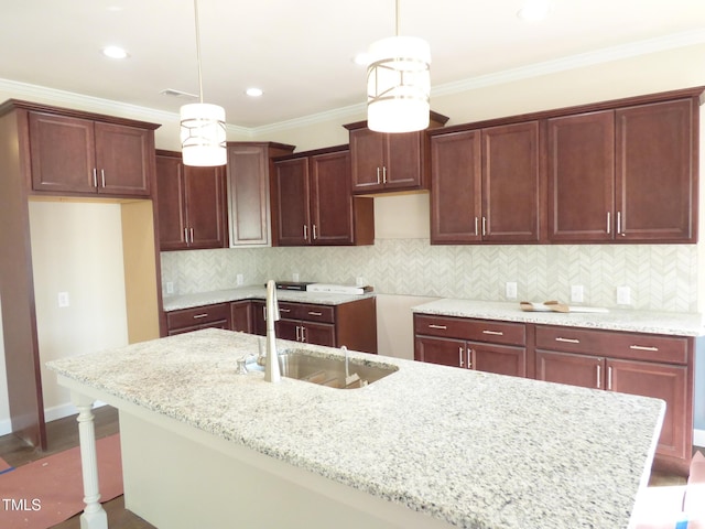 kitchen featuring pendant lighting, a kitchen island with sink, sink, and light stone countertops