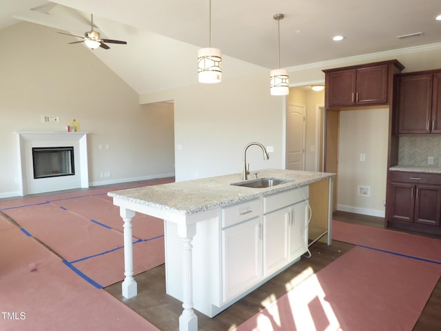 kitchen featuring pendant lighting, sink, light stone counters, white cabinets, and vaulted ceiling