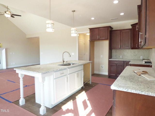 kitchen featuring pendant lighting, tasteful backsplash, sink, light stone countertops, and a center island with sink