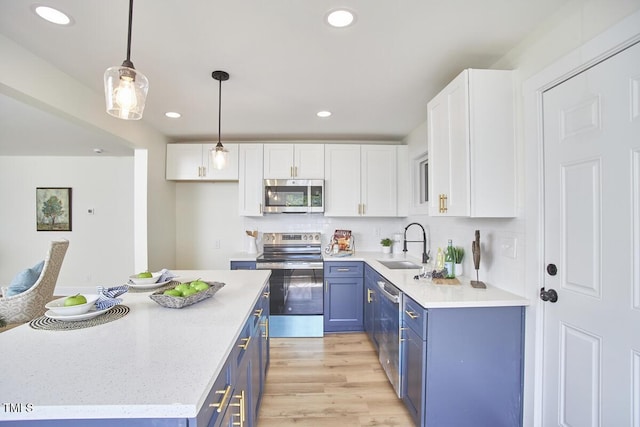 kitchen with appliances with stainless steel finishes, decorative light fixtures, blue cabinets, white cabinetry, and light hardwood / wood-style flooring