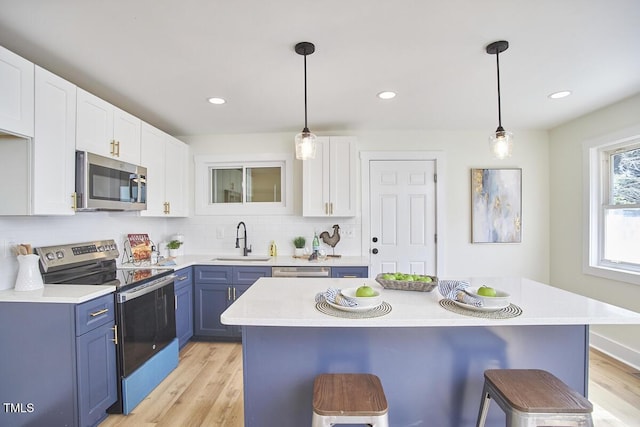 kitchen featuring decorative light fixtures, blue cabinets, sink, white cabinets, and stainless steel appliances