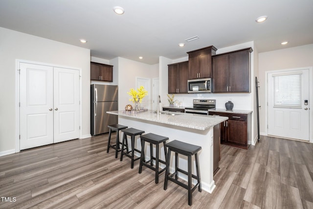 kitchen with stainless steel appliances, hardwood / wood-style flooring, a kitchen island with sink, and a kitchen bar