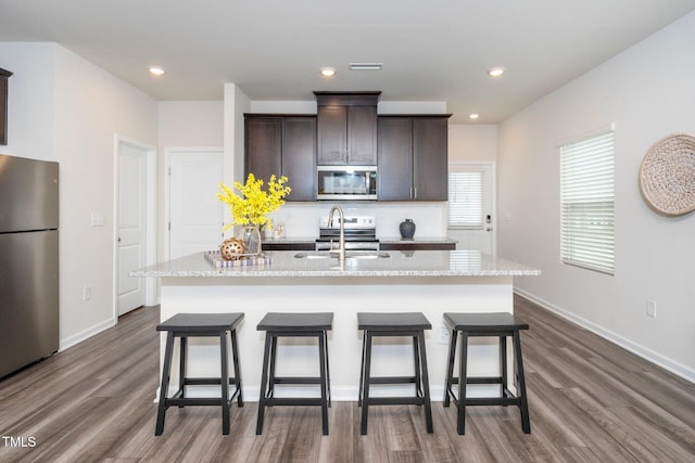 kitchen with appliances with stainless steel finishes, hardwood / wood-style floors, an island with sink, sink, and dark brown cabinets