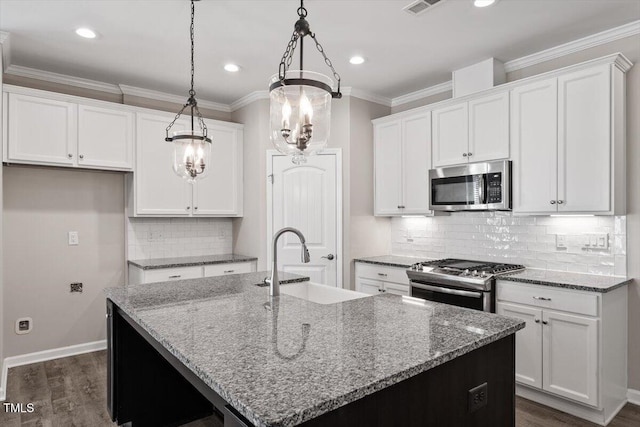 kitchen with white cabinetry, stainless steel appliances, decorative light fixtures, and an island with sink