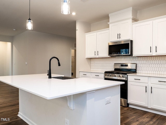 kitchen featuring appliances with stainless steel finishes, a center island with sink, pendant lighting, sink, and white cabinetry