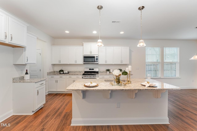 kitchen with decorative light fixtures, a center island with sink, white cabinets, and appliances with stainless steel finishes