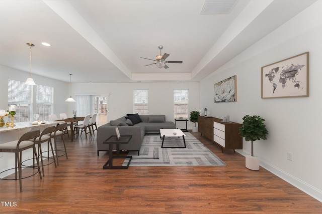 living room with dark wood-type flooring, ceiling fan, and a raised ceiling