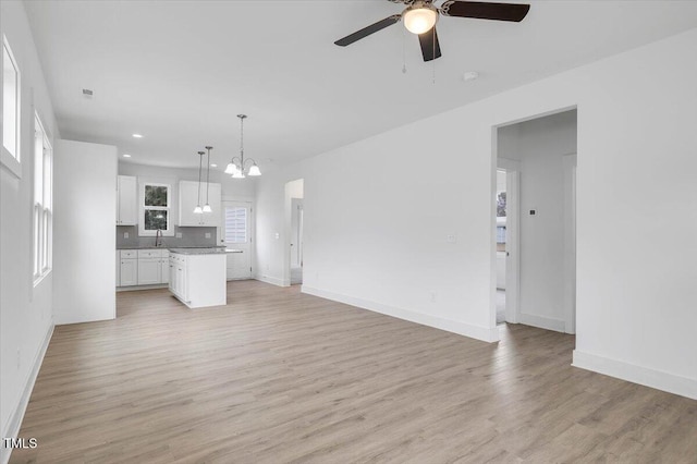 unfurnished living room featuring sink, ceiling fan with notable chandelier, and light wood-type flooring