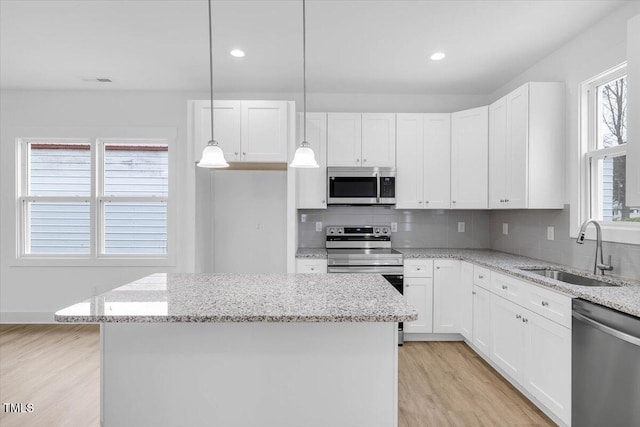 kitchen featuring a kitchen island, white cabinetry, appliances with stainless steel finishes, and decorative light fixtures