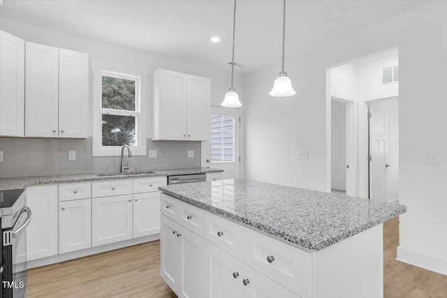 kitchen featuring sink, white cabinetry, a center island, hanging light fixtures, and light stone countertops