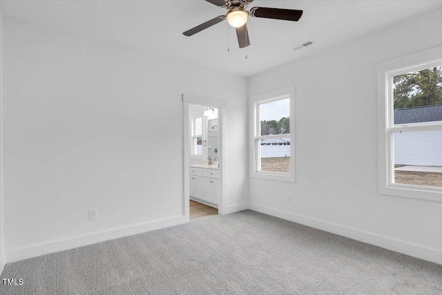 unfurnished bedroom featuring multiple windows, ceiling fan, light colored carpet, and ensuite bath