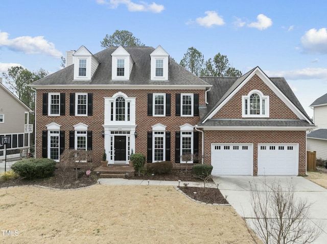 colonial home featuring an attached garage, brick siding, driveway, roof with shingles, and a front yard