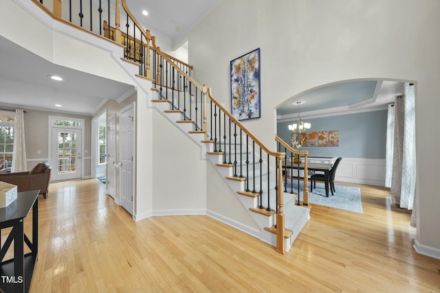 stairway featuring arched walkways, a high ceiling, wood finished floors, wainscoting, and crown molding