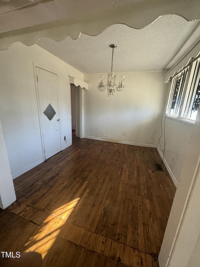 unfurnished dining area with a notable chandelier, dark hardwood / wood-style floors, and a textured ceiling