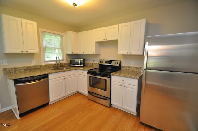 kitchen with sink, light hardwood / wood-style flooring, stone counters, white cabinetry, and stainless steel appliances