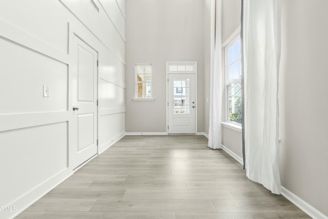 entryway featuring a healthy amount of sunlight, light wood-type flooring, and a towering ceiling