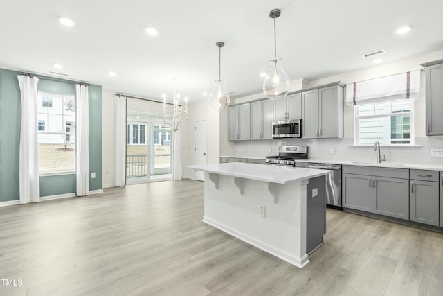 kitchen featuring sink, gray cabinetry, hanging light fixtures, stainless steel appliances, and a kitchen island